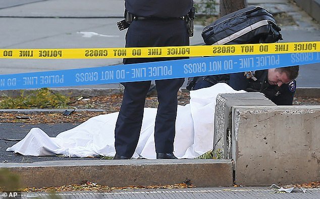 A paramedic looks at a body covered by a white sheet along a bike path after the riot