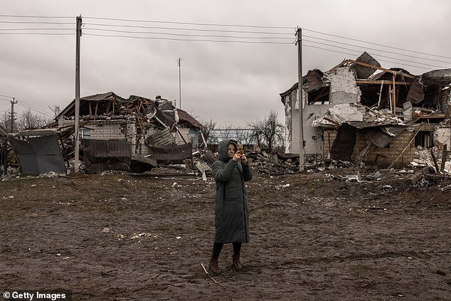 A woman takes photos with her mobile phone next to ruined houses after Russian missile attacks