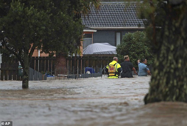 Emergency workers and a man walk through floodwaters in Auckland on Friday.
