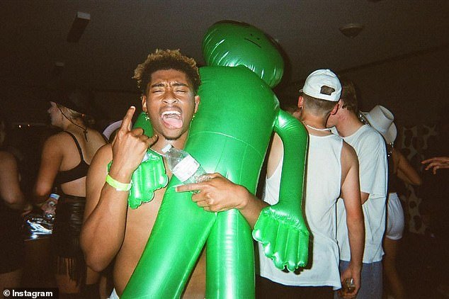 Stills show Washington partying with friends and posing for the camera, while another shows him topless and clutching an inflatable alien.