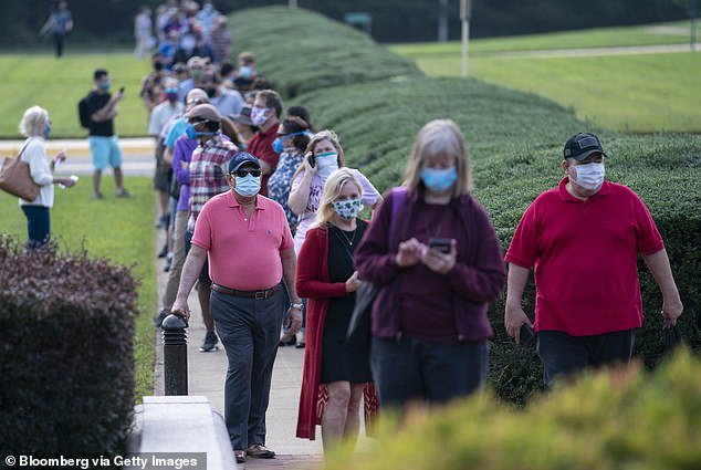 Americans wear masks while waiting in line to vote in the 2020 presidential election. Some colleges and businesses are reinstating mask mandates as Covid cases rise in the United States