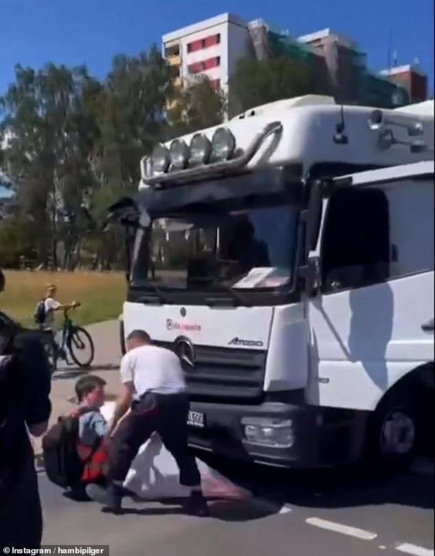 The photo shows the driver trying to drag the protester sitting on the road from under the truck
