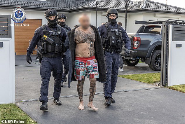 The heavily tattooed head of the Lone Wolf outlaw motorcycle gang, Medhat Mankaryous (pictured centre), was marched from his premises by NSW Police officers during an early morning raid on Friday.