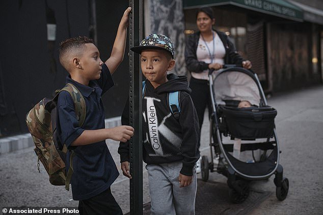 There are now nearly 60,000 migrants in the care of the city, and about 21,000 new migrant children will be attending school this year.  Ecuadorian migrant Kimberly Carchipulla (right) and her son, 5-year-old Damien, center, wait for the bus on their way to school in New York on Thursday