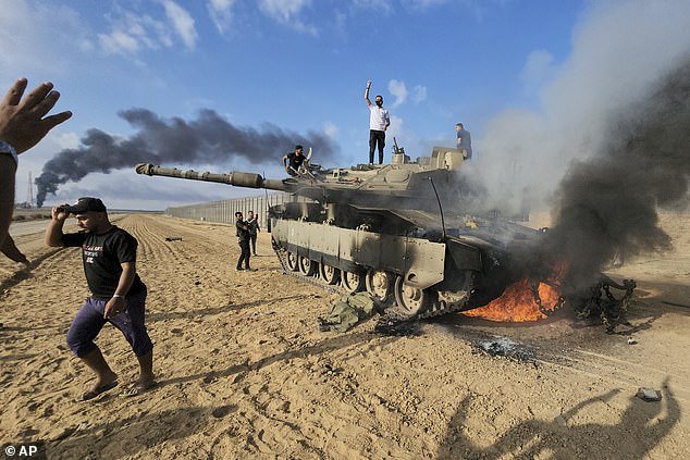 Palestinians celebrate at a destroyed Israeli tank at the Gaza Strip fence on Saturday afternoon