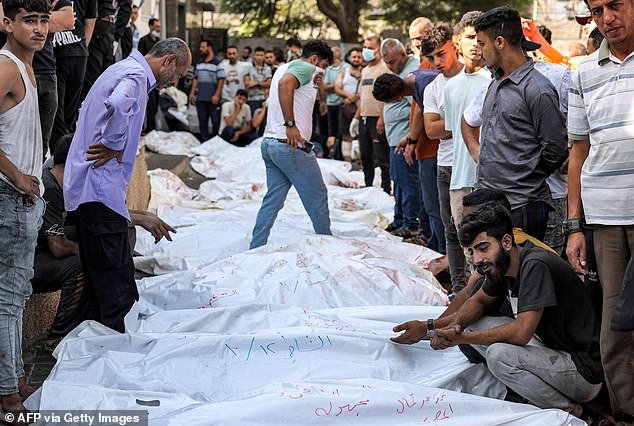 People stand near the bodies of victims of Israeli airstrikes outside al-Shifa hospital morgue in Gaza City on Thursday