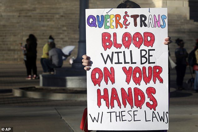 A protester outside the Kansas Statehouse holds a sign after a rally on Transgender Day of Visibility as schools grapple with gender identity issues