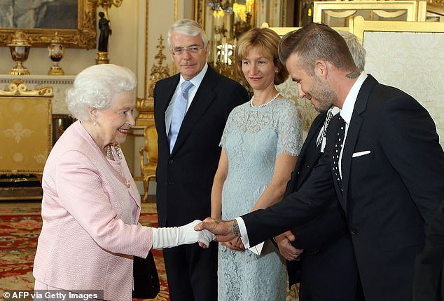 David Beckham bows his head as he shakes hands with the Queen as John Major looks on