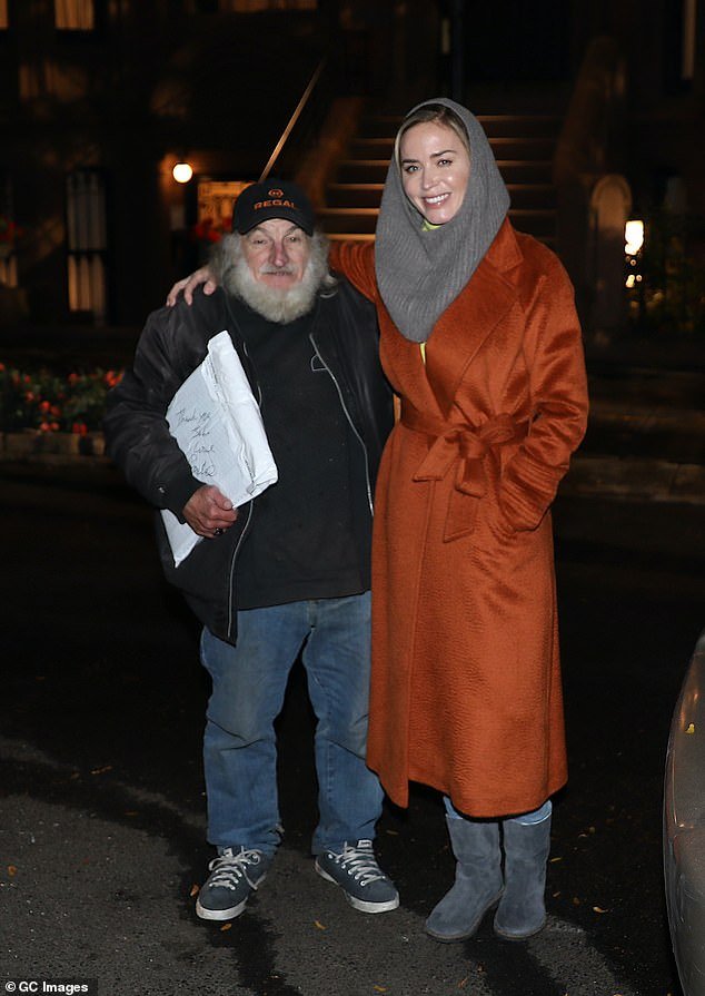 Staying warm: She covered her blonde locks with a gray headband as she attended the nighttime shoot (pictured with a member of the crew)