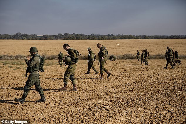 Israeli soldiers walk in a field as they search for body remains and personal items left behind after the deadly Hamas attack on Israel's southern border on November 17