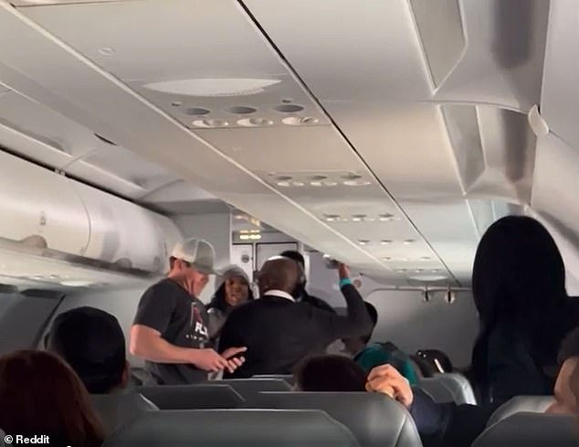 A woman in a gray cap joined the fray and tried to mediate and talk to the distraught passenger