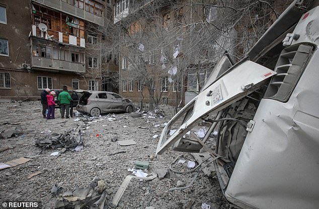 Local residents stand outside their apartment building and cars damaged during a Russian missile attack in Kharkiv, Ukraine on Friday