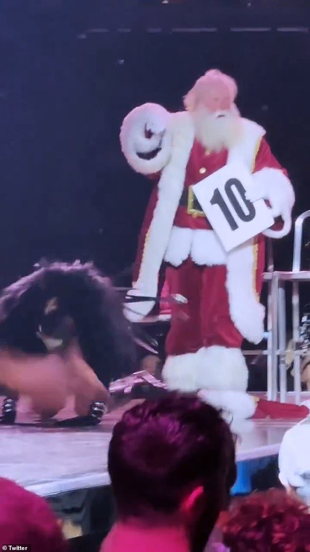 The person dressed as Santa Claus sat on a chair in the center of the stage while Madonna performed nearby