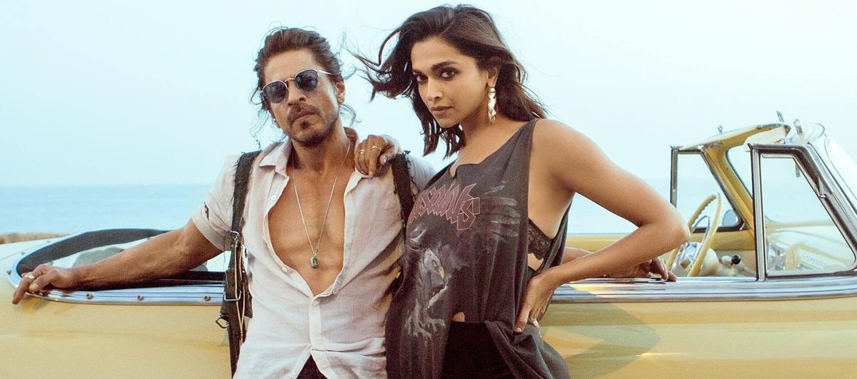 Shah Rukh Khan and Deepika Padukone lean against a yellow convertible as they look stunningly hot in Pathaan.  They look like they saw you from across the bar and liked your vibe.