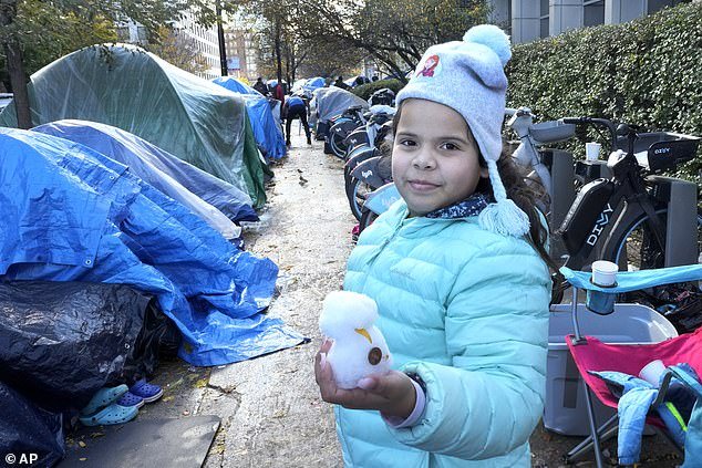 A young migrant girl eagerly shows off what she's made of overnight snowfall in a small tent community in Chicago