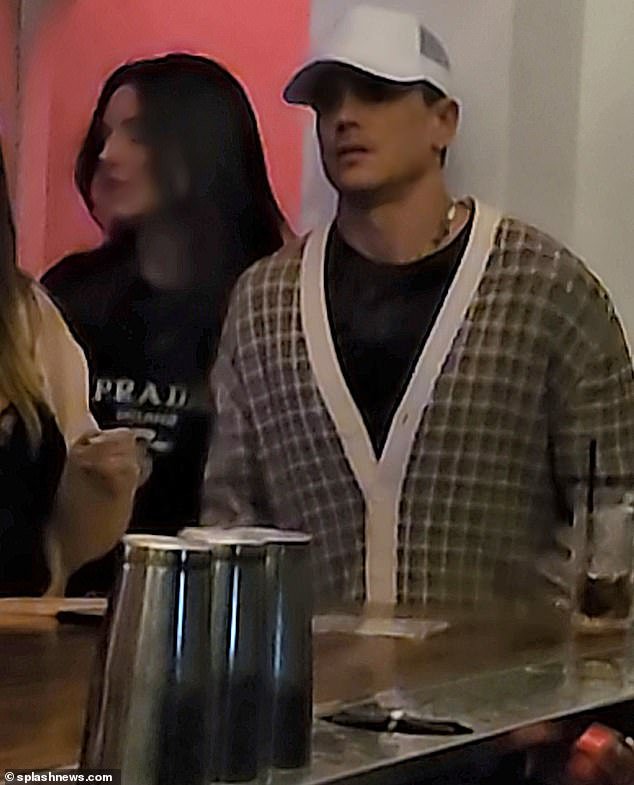 The reality star looked dapper in a black and white cardigan over a black T-shirt.  He was clean shaven and wore a white beaked cap over his dark hair