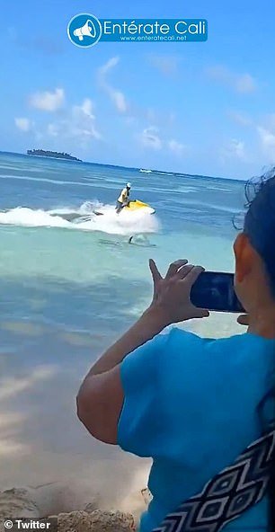 A tourist worker on a jet ski tries to scare off the shark