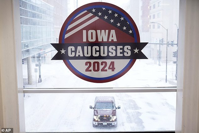 A pickup truck drives down a snowy road under a sign in the Iowa Caucus on Friday