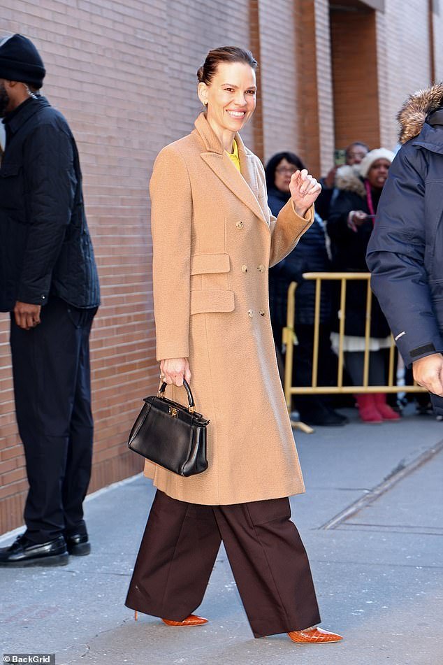 The Oscar-winning actress beamed as she donned a long beige coat with merlot red pants and orange heels