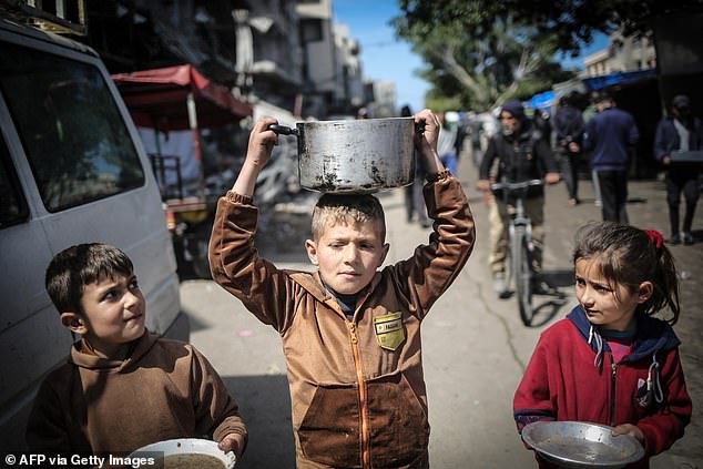 Children carry kitchen utensils as they walk to a food distribution point in Gaza