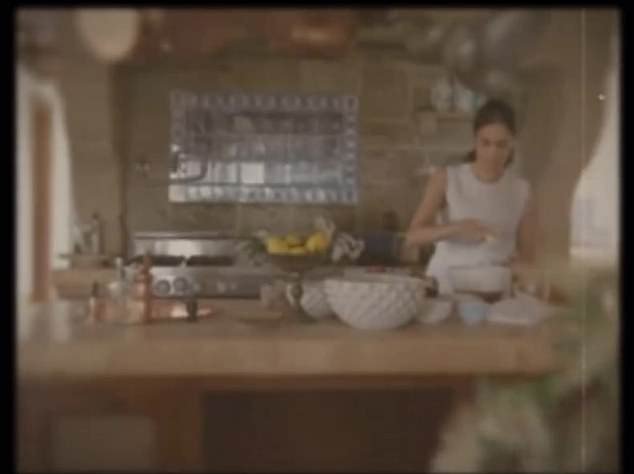 It then fades away to reveal Meghan cooking in a beautiful kitchen, with copper pans hanging above her head as she waves