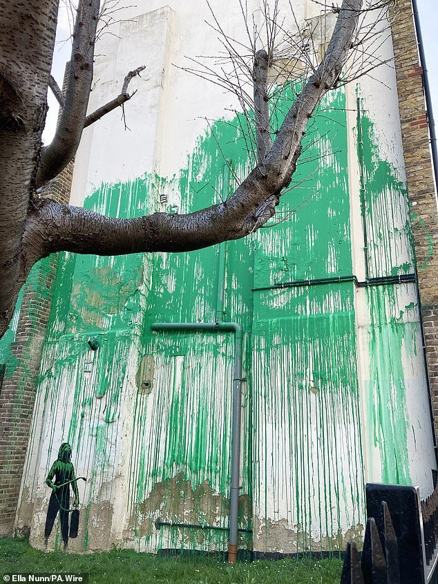 The artwork features a splash of green painted behind a bare tree to resemble foliage, alongside a stencil of a person holding what appears to be a pressure hose.