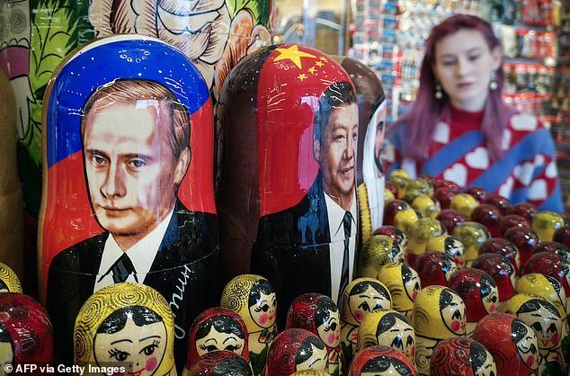 A seller stands next to traditional Russian wooden nesting dolls, Matryoshka dolls, depicting Russian President Vladimir Putin (L) and his Chinese counterpart Xi Jinping