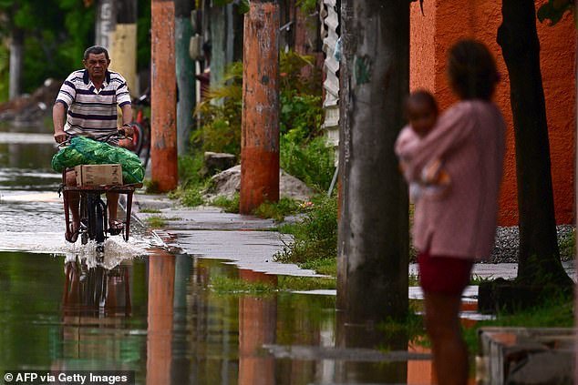 A man cycles through a flooded street after a rainstorm in the Uruai district of the city of Duque de Caxias,