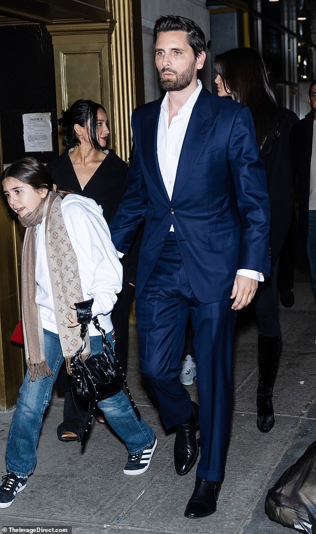 Scott looked dapper in a deep blue suit and a crisp white shirt with the top buttons undone;  there were two women standing behind him, including occasional girlfriend Bella Banos