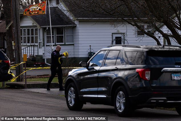 An officer rolls out police tape Wednesday as the investigation into the quadruple homicide continues