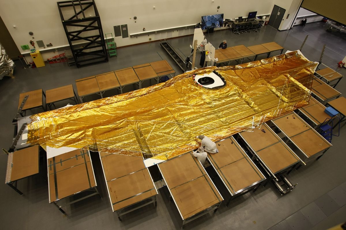 A gold five-layer sunshade stretched over a piece of the James Webb Space Telescope lying on the floor