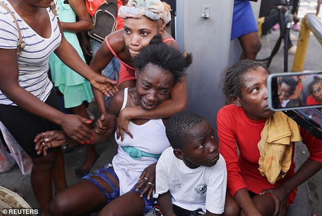 A woman is comforted by others at a crime scene where the bodies of several people shot dead earlier this morning amid an escalation of gang violence were removed by ambulance in Port-au-Prince