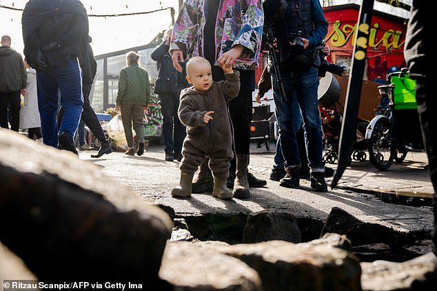 A toddler in boots watches as locals take to the streets in the former hippie community, home to about 250 children