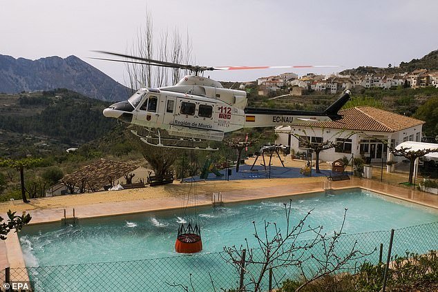 A helicopter is filled with water from a swimming pool as crews work to fight the fire