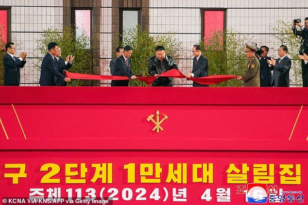 Kim was then seen wearing his current favorite black leather bomber jacket as he used scissors to cut the red ribbon (pictured) while standing on a large stage decorated with communist red ribbons and adorned with a gold hammer and sickle.