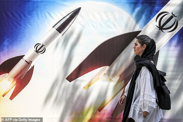 A woman walks past a banner showing the launch of missiles with the emblem of the Islamic Republic of Iran in central Tehran on April 15, 2024