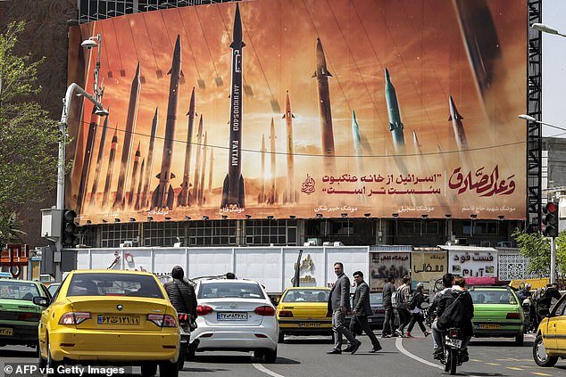 Motorists drive their vehicles past a billboard depicting Iranian ballistic missiles in use, with text in Arabic 