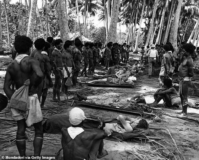 Local people look at wounded American soldiers.  and Australian soldiers are placed on a row of stretchers.  Papua New Guinea, December 1942