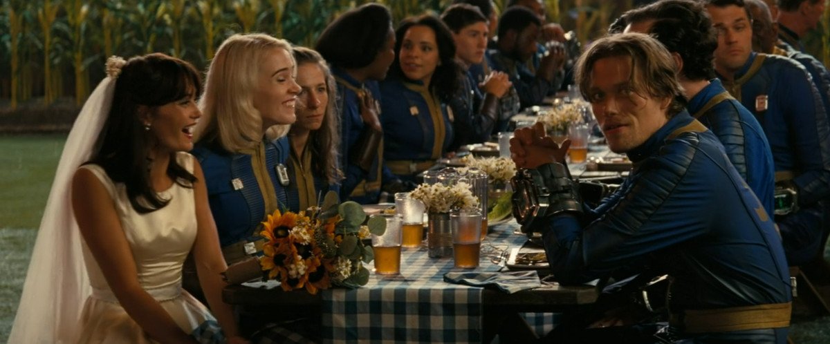 Ella Purnell, wearing a wedding dress, laughs as the rest of the wedding party chats at a table in Fallout
