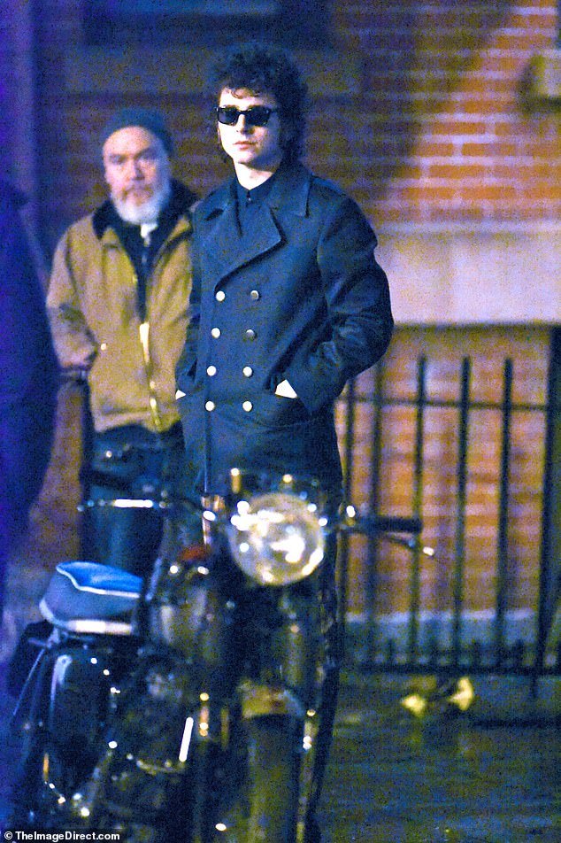 The actor was seen standing among a bearded extra in jeans and a brown jacket with a gray toque and a scooter parked on the street in front of the scene.