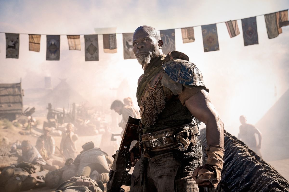 Djimon Hounsou as General Titus in Rebel Moon - Part Two: The Scargiver holds a gun at his side as he stands near a slaughtered village
