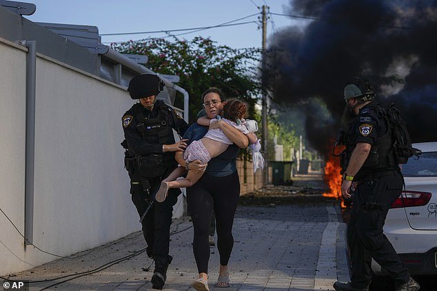 Israeli police officers evacuate a woman and a child from a site hit by a rocket fired from the Gaza Strip, in Ashkelon, southern Israel, Saturday, October 7, 2023