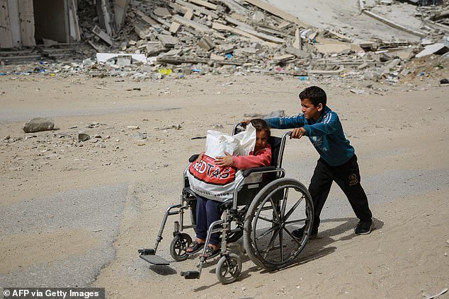 A boy pushes a young girl in a wheelchair past a destroyed building in Gaza City on March 28