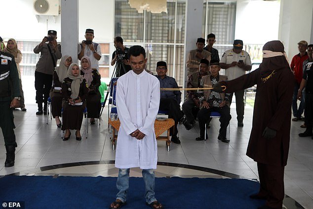 A man from Aceh stands firmly on a blue mat while being caned