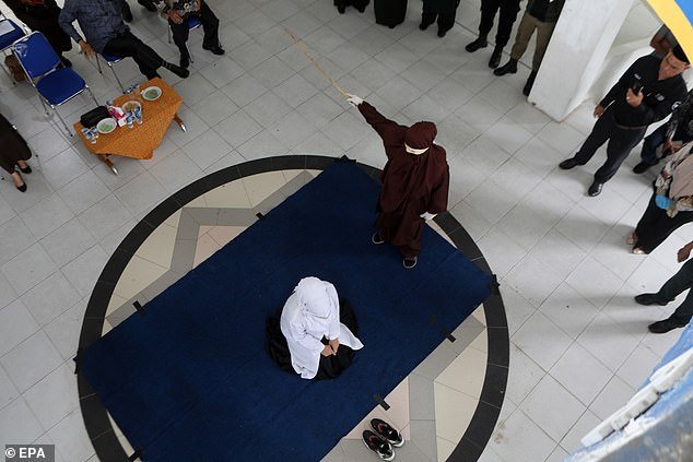 One of the women who was caned kneels in front of her wearing shoes as she anticipates her punishment