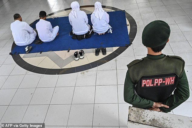 An officer watches over two couples awaiting caning by Sharia police as punishment for forbidden relations with the opposite sex