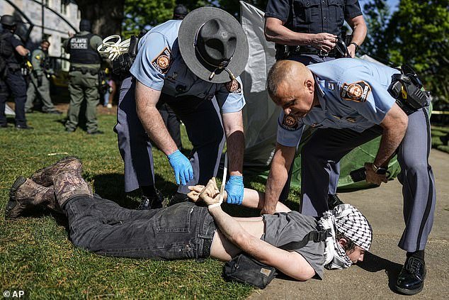 A protester wearing a keffiyeh is pinned to the ground as officers place cable ties around his wrist
