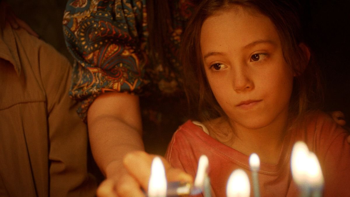 A young girl looks sullen at a cake with lit candles.