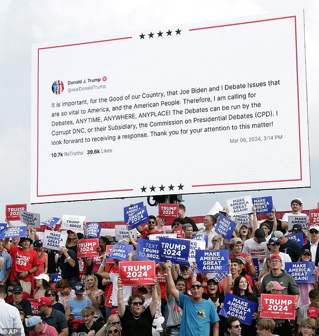 Supporters hold signs as a message is shown on a large video screen stating that former President Donald Trump will debate President Joe Biden anytime, anywhere