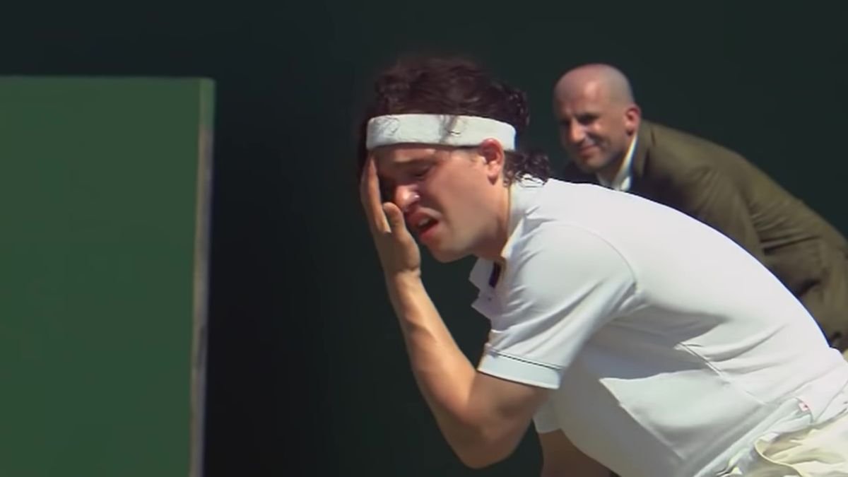 Kit Harington wipes sweat from his face with a pained expression, dressed in tennis gear in 7 Days in Hell